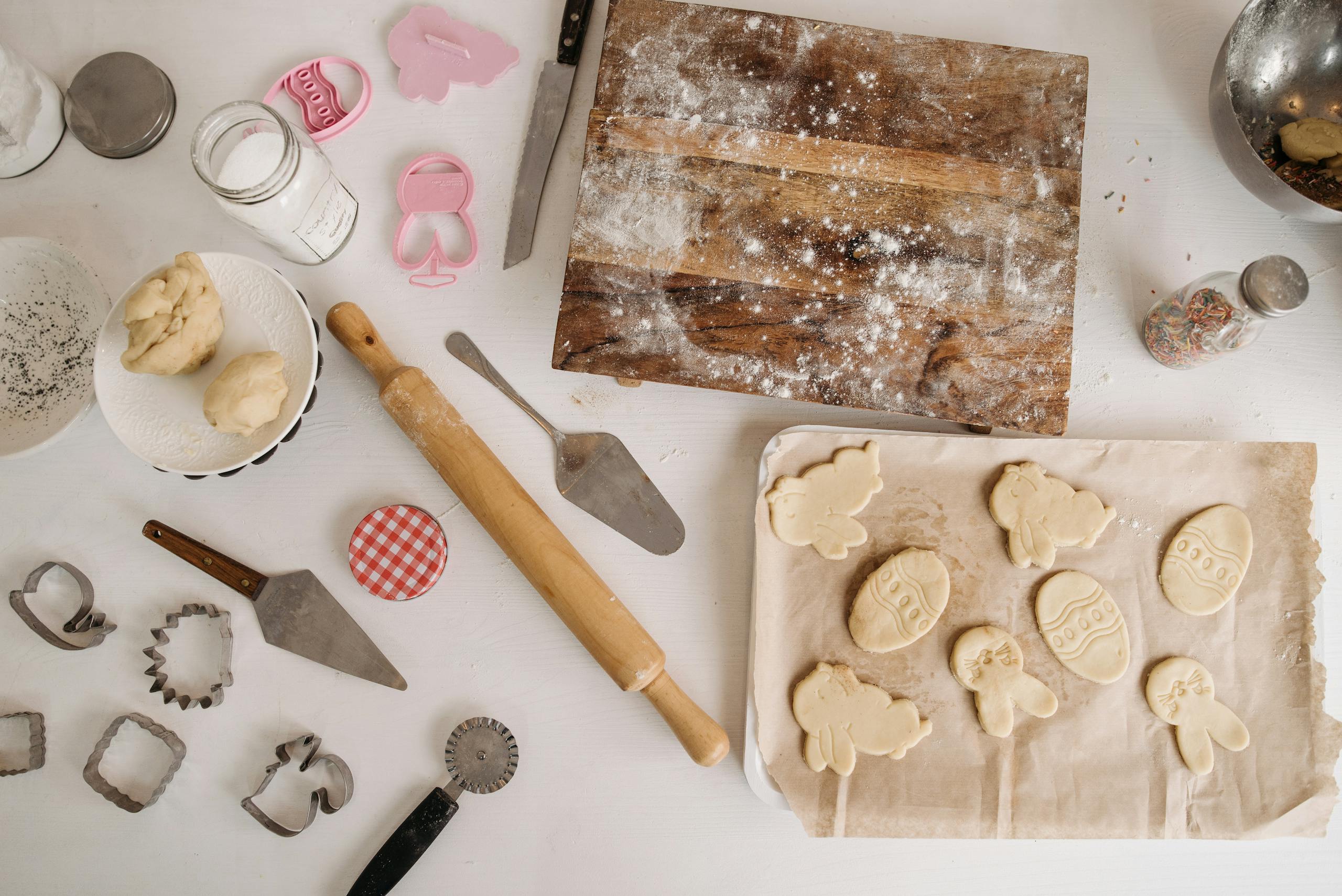 Top view of baking preparation with dough, cookie cutters, and utensils on a floured surface.